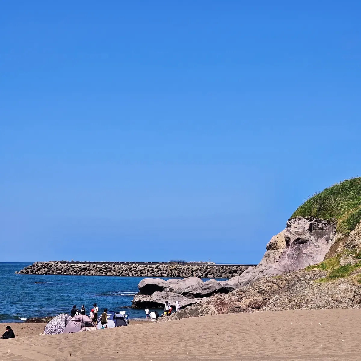 青空の下の砂浜と、すぐそばの岩場