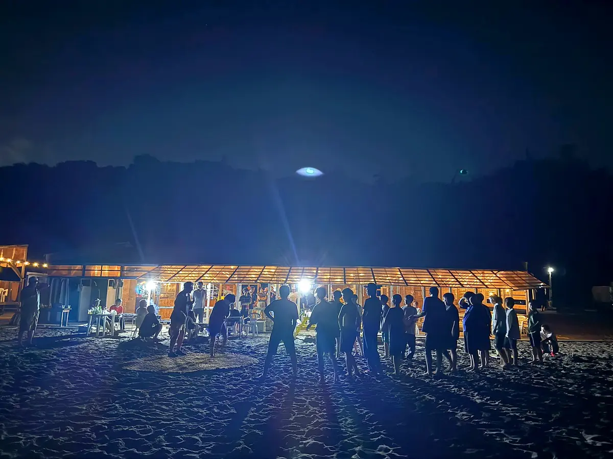 灯りのともる店内と、夜の砂浜に集まる人たち