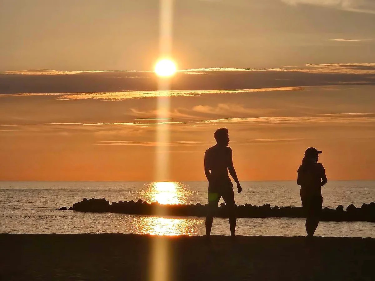 日本海に沈む夕日と、夕暮れの浜辺を歩く人のシルエット