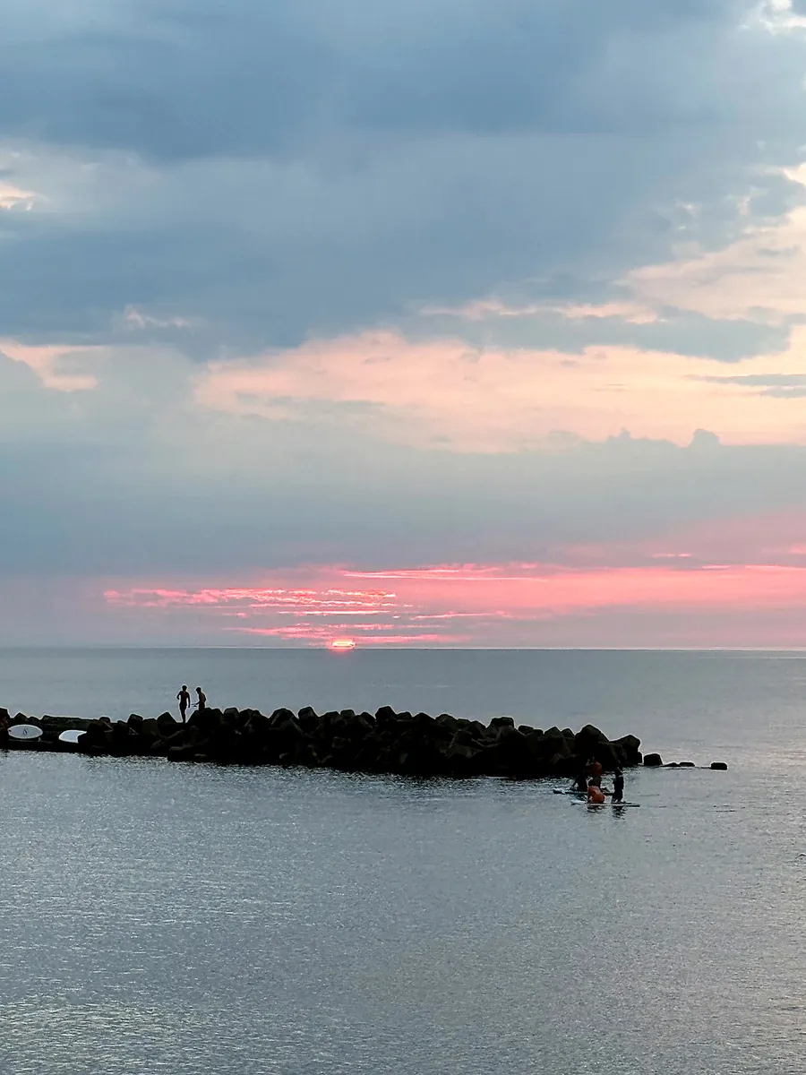夕焼けに染まる空の下、海に浮かぶSUPと堤防のシルエット