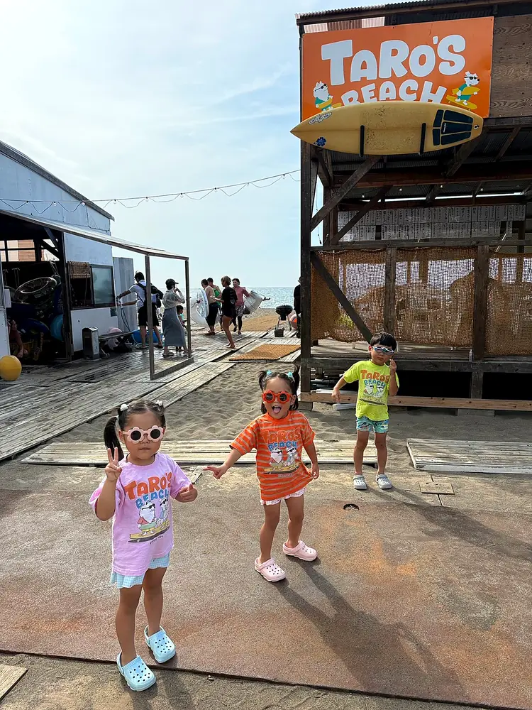タローズビーチの看板の前で、ロゴTシャツを着てポーズをとる子どもたち